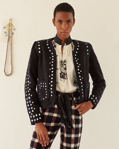 A stylish person poses confidently, sporting the Billie Midnight Mirror Jacket, featuring a black design with white polka dots, paired with a white patterned blouse and plaid pants. Hand-embroidered mirrors catch the light from the necklace hanging on the wall in the background. Mirror Jacket, Embellished Jacket, Hand Making, Woven Cotton, Cotton Weaving, Cosmos, Vest Jacket, Hand Woven, Hand Embroidered