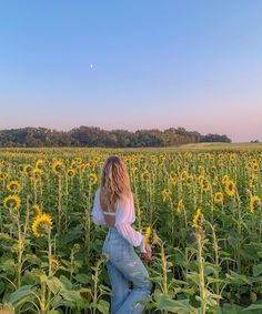 a woman standing in the middle of a field of sunflowers looking at the sky