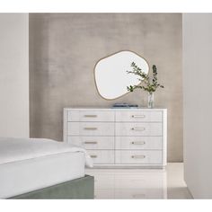 a white dresser with a mirror on top and a plant in the corner next to it