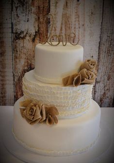 a three tiered white cake with brown flowers on the top and one layer is decorated with burlap