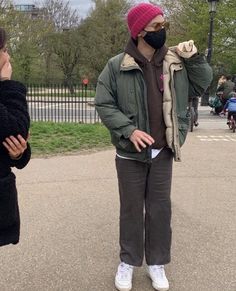 two people standing in the street wearing face masks and talking on their cell phones while one woman holds her hand up to her ear