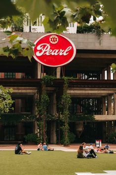 people sitting on the grass in front of a building with a sign that reads dear