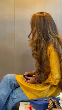 a woman with long hair sitting on a table looking at her cell phone