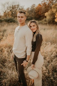 a young man and woman standing in tall grass holding each other's hands while posing for the camera