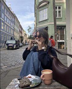 a woman sitting on a bench eating food and drinking coffee