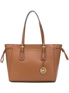 Brown leather Voyager medium tote bag from Michael Michael Kors featuring round top handles, a top zip fastening, a gold-tone logo plaque and a logo tag. Gold Shoulder Bag With Logo Hardware For Shopping, Everyday Gold Bag With Metal Logo, Gold Tote Bag With Logo Hardware, Everyday Gold Bags With Metal Logo, Gold Bags With Metal Logo For Everyday Use, Gold Travel Bags With Logo Hardware, Elegant Tote Bag With Logo Hardware, Luxury Brown Shoulder Bag With Metal Logo, Gold Office Bags With Metal Logo