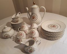 a white table topped with lots of dishes and cups next to each other on top of a cloth covered table