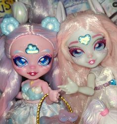 two dolls are sitting next to each other on a bed with pink hair and blue eyes