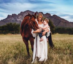 a woman holding a baby next to a horse