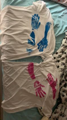 two shirts with hand prints on them laying on a bed