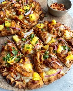 a pizza with pineapple, onions and other toppings sitting on a wooden cutting board