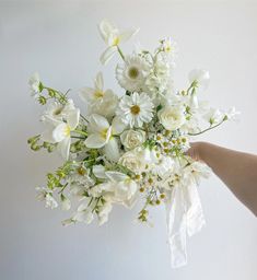 a bouquet of white flowers is held up by someone's hand against a wall