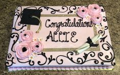 a pink and black graduation cake with flowers on the top, congratulations all 3 written in white