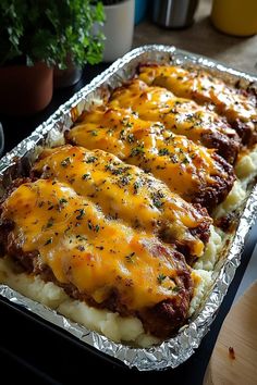 baked meat and cheese covered potatoes in a baking pan on a table with a potted plant