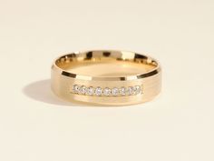 a yellow gold wedding band with channeled diamond set in the center, on a white background