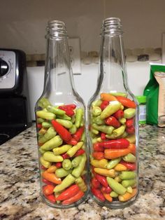 two glass bottles filled with pickles on top of a counter