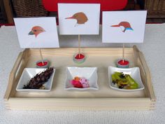 three little birds are sitting in small bowls on a tray with two cards and one doll