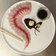 a white plate topped with sushi and chopsticks next to a bowl of sauce