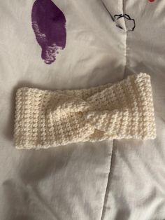 a crocheted headband laying on top of a white bed with purple ink