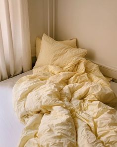 an unmade bed with yellow sheets and pillows