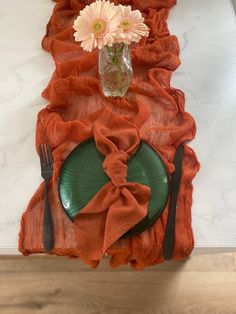 the table is set with an orange linen runner and green plates, silverware, and flowers in a vase