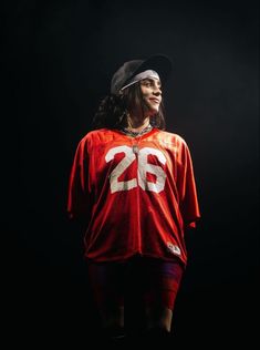 a man in a red jersey and hat standing on a black background with his hands behind his back