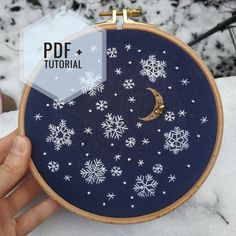 someone is holding up a embroidery project with snowflakes and a crescent on it