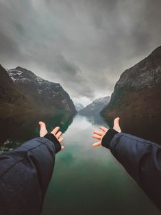 someone is holding their hands out in front of the camera as they look down at a body of water