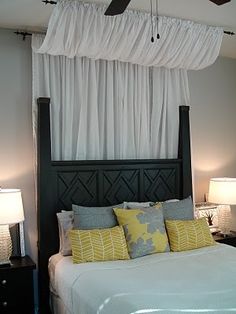 a bedroom with a ceiling fan and white drapes on the window over the bed