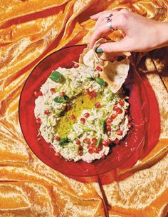 a red plate topped with guacamole and tortilla chips next to a woman's hand