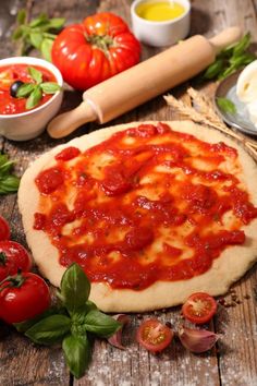 a pizza sitting on top of a wooden table covered in sauce and toppings next to tomatoes