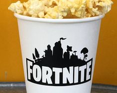 a white bucket filled with popcorn sitting on top of a metal table next to a yellow wall