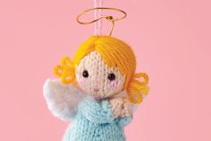 a crocheted angel ornament hanging from a string on a pink background