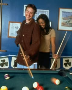 a man and woman standing next to a pool table with cues in front of them