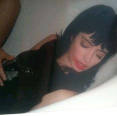 a woman laying down in a bathtub with her eyes closed and holding a bottle