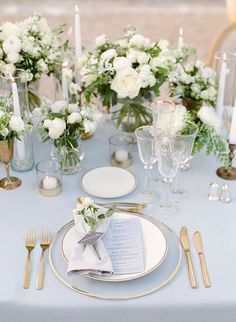 the table is set with white flowers and silverware, gold rimmed plates and napkins