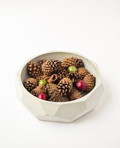 a white bowl filled with pine cones and berries