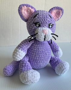 a crocheted purple cat sitting on top of a table next to a white wall