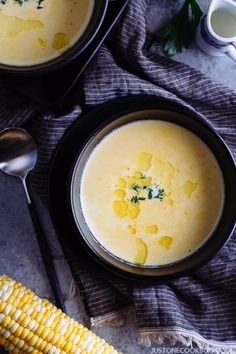 two bowls filled with corn on the cob next to a spoon and cup of milk