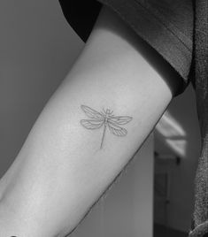 a small dragonfly tattoo on the left inner arm and lower arm, it appears to be in black and white