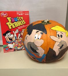 a pumpkin painted to look like cartoon characters next to a box of fruity pebbles