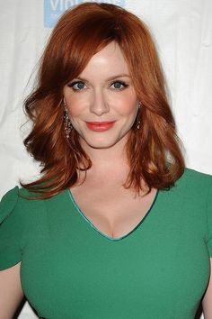 a woman with red hair and blue eyes posing for the camera in a green dress