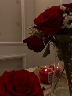 red roses in a vase on a table with two votive candles next to it