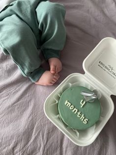 a baby laying on top of a bed next to a container with a cake in it