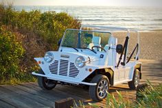 a white jeep parked on top of a wooden ramp next to the ocean and grass