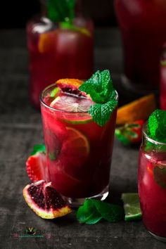 two glasses filled with blood orange and mint garnish next to sliced grapefruit