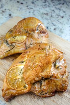 two pieces of chicken on a cutting board with lemon slices and rosemary garnish