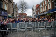 a crowd of people standing next to each other on a sidewalk near buildings and shops