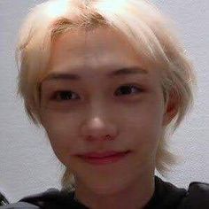 a young man with blonde hair wearing a black shirt and looking at the camera while standing in front of a white wall