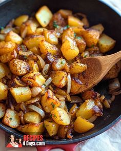 a skillet filled with potatoes and onions on top of a white cloth next to a wooden spoon